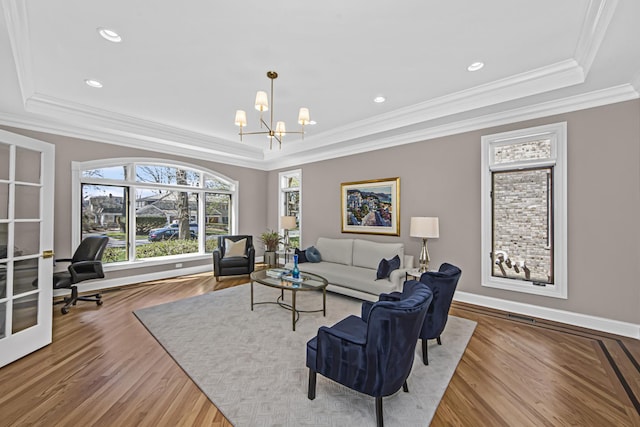 living room with a notable chandelier, a tray ceiling, wood-type flooring, and ornamental molding