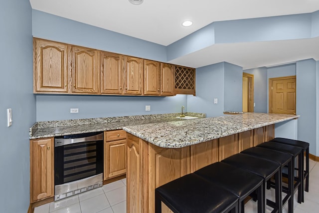 kitchen with wine cooler, light stone counters, a breakfast bar, and light tile patterned flooring