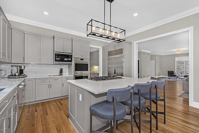 kitchen featuring a kitchen island, a breakfast bar area, gray cabinetry, ornamental molding, and built in appliances