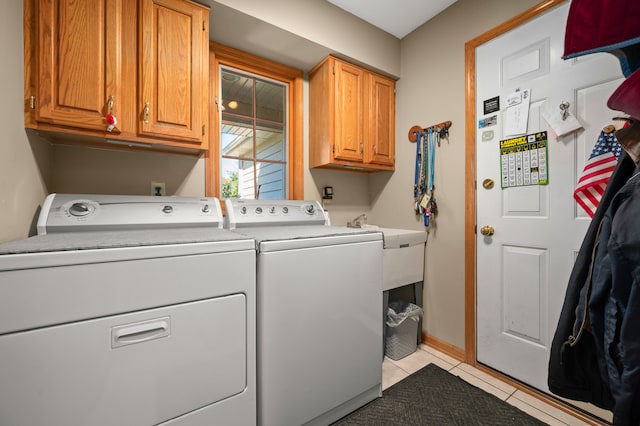 clothes washing area featuring washer and clothes dryer, light tile patterned floors, and cabinets