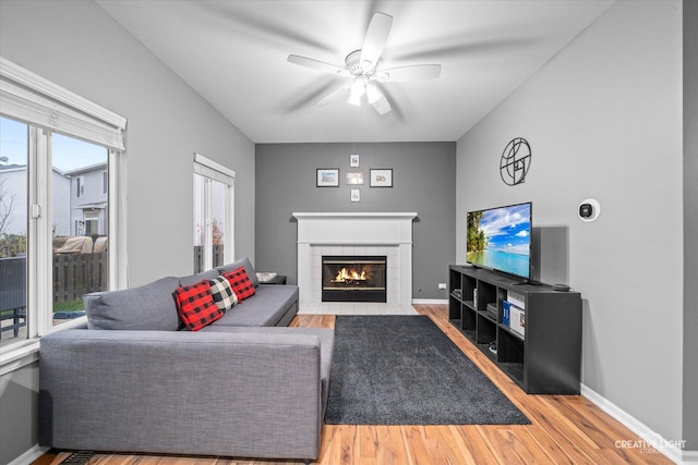 living room featuring ceiling fan, wood-type flooring, and a tiled fireplace