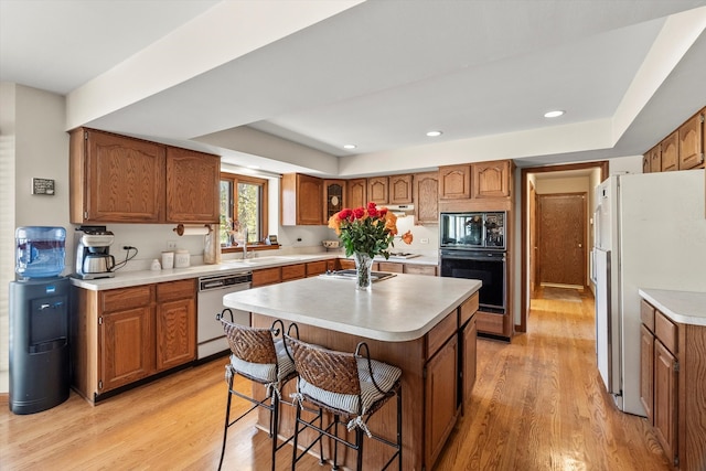 kitchen featuring a breakfast bar, white appliances, a raised ceiling, light hardwood / wood-style flooring, and an island with sink