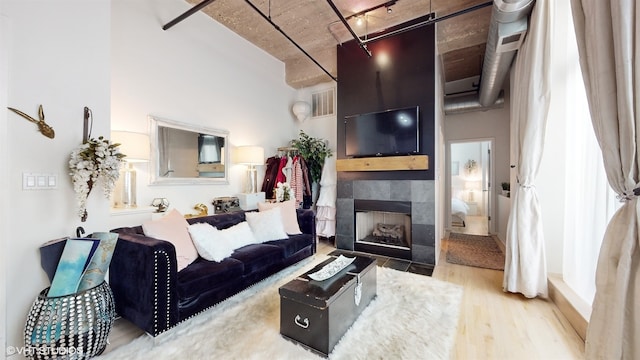 living room with a tile fireplace, wood-type flooring, and a high ceiling