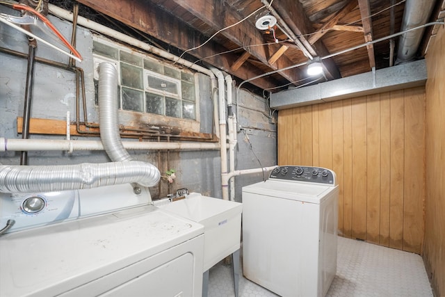 clothes washing area featuring independent washer and dryer, wooden walls, and sink