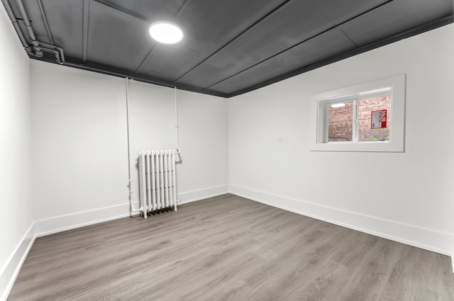 basement featuring light wood-type flooring, ornamental molding, and radiator