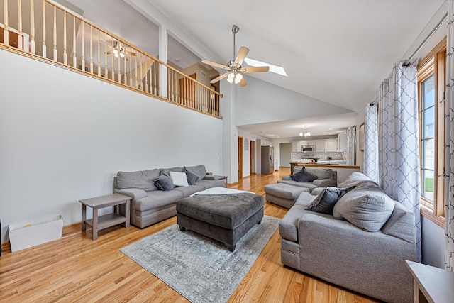 living room featuring a skylight, ceiling fan, high vaulted ceiling, and light hardwood / wood-style floors