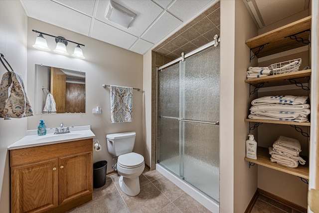 bathroom with a paneled ceiling, vanity, tile patterned flooring, toilet, and a shower with shower door