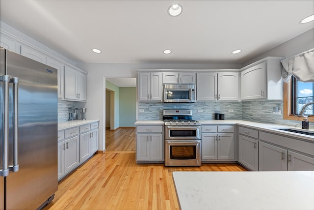 kitchen with sink, backsplash, gray cabinets, appliances with stainless steel finishes, and light wood-type flooring