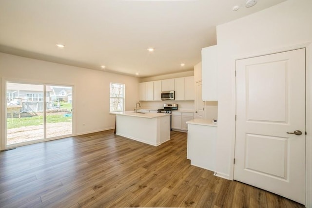 kitchen with appliances with stainless steel finishes, a kitchen island with sink, sink, hardwood / wood-style flooring, and white cabinetry