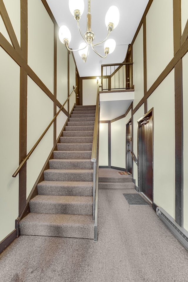 stairs with carpet flooring, a chandelier, a baseboard heating unit, and ornamental molding