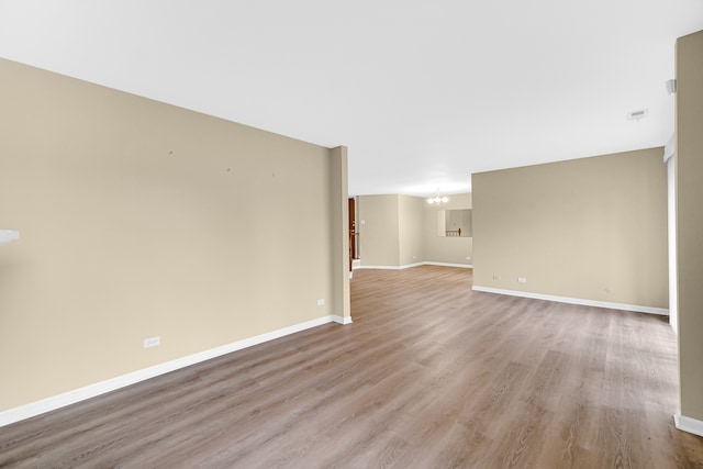 unfurnished room featuring a notable chandelier and light wood-type flooring