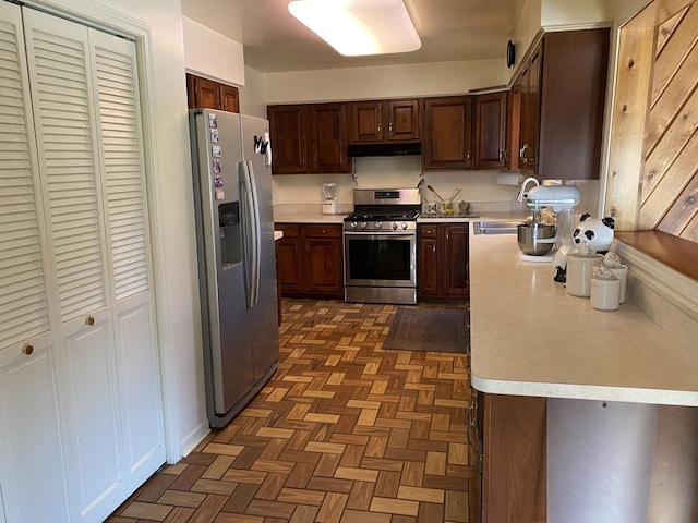 kitchen with wood walls, dark parquet floors, sink, dark brown cabinets, and stainless steel appliances