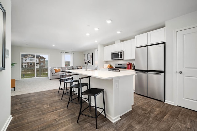 kitchen featuring a breakfast bar, stainless steel appliances, white cabinets, dark hardwood / wood-style floors, and an island with sink