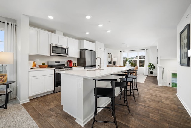 kitchen featuring a kitchen breakfast bar, dark hardwood / wood-style flooring, stainless steel appliances, a center island with sink, and white cabinetry