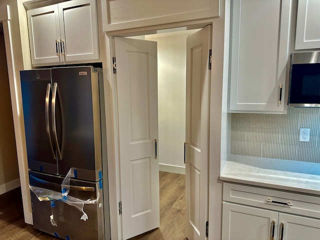 kitchen with light stone countertops, stainless steel appliances, white cabinetry, and light hardwood / wood-style floors