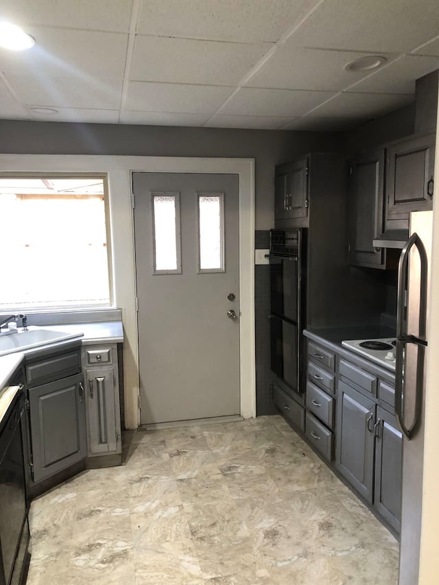 kitchen with a paneled ceiling, gray cabinetry, sink, black appliances, and range hood