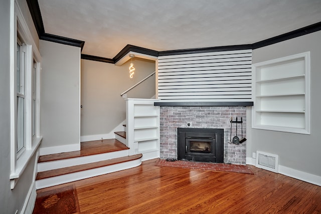 unfurnished living room featuring hardwood / wood-style floors, built in shelves, crown molding, and a brick fireplace