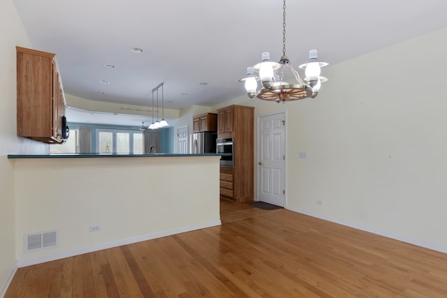 kitchen with kitchen peninsula, appliances with stainless steel finishes, decorative light fixtures, a chandelier, and light hardwood / wood-style floors