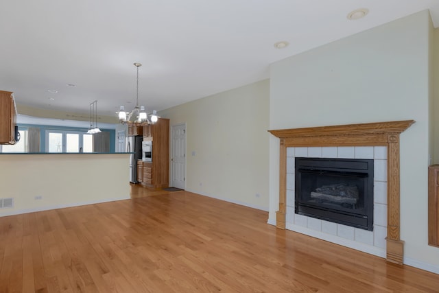 unfurnished living room featuring a tiled fireplace, an inviting chandelier, and light wood-type flooring