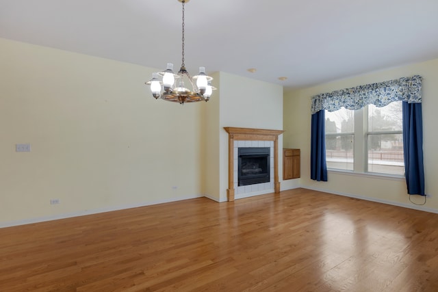 unfurnished living room featuring a tile fireplace, hardwood / wood-style floors, and a notable chandelier