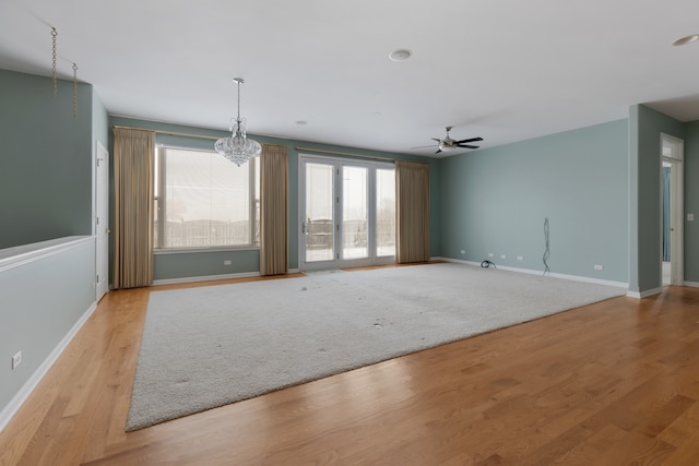 unfurnished living room with ceiling fan with notable chandelier and light hardwood / wood-style floors