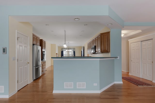 kitchen with hanging light fixtures, light hardwood / wood-style flooring, kitchen peninsula, a chandelier, and appliances with stainless steel finishes