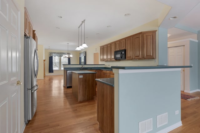 kitchen with an inviting chandelier, kitchen peninsula, light hardwood / wood-style floors, decorative light fixtures, and appliances with stainless steel finishes