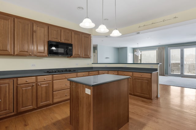 kitchen with a kitchen island, black appliances, decorative light fixtures, and light hardwood / wood-style floors