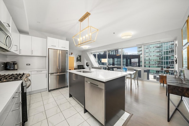 kitchen with stainless steel appliances, sink, decorative light fixtures, white cabinets, and an island with sink