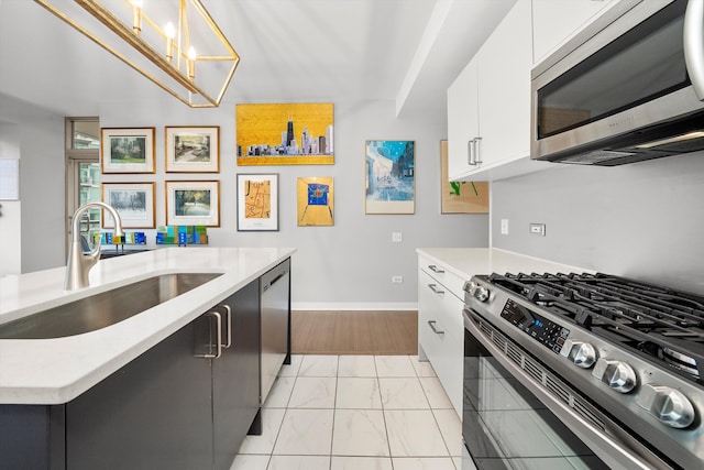 kitchen featuring light wood-type flooring, stainless steel appliances, sink, decorative light fixtures, and white cabinets