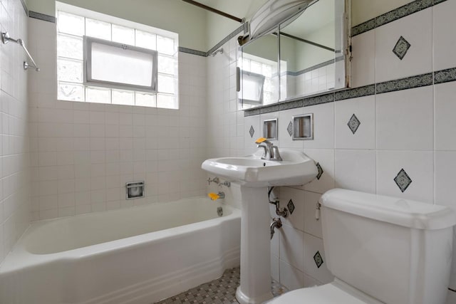 bathroom with tile patterned floors, tiled shower / bath, tile walls, and toilet