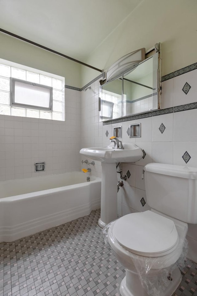 bathroom with tile patterned flooring, tiled shower / bath combo, toilet, and tile walls