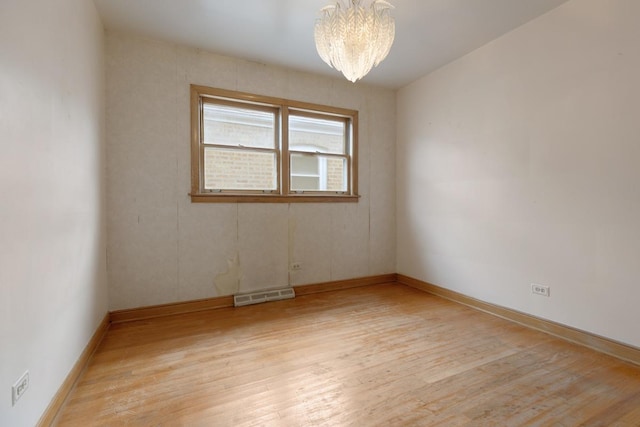 spare room featuring light wood-type flooring and an inviting chandelier