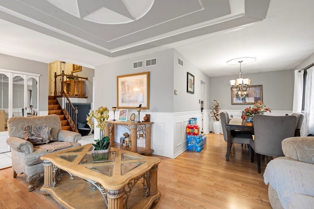 living room with light wood-type flooring, a tray ceiling, and an inviting chandelier