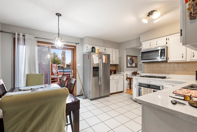 kitchen with hanging light fixtures, tasteful backsplash, light tile patterned flooring, white cabinetry, and stainless steel appliances