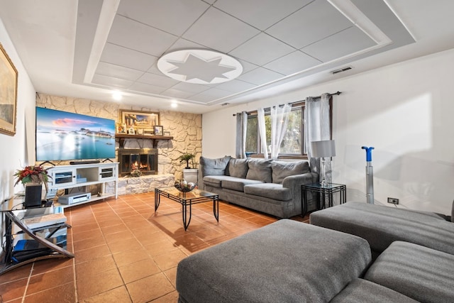 tiled living room featuring a raised ceiling and a stone fireplace