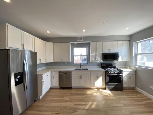 kitchen with sink, white cabinets, stainless steel appliances, and light hardwood / wood-style floors