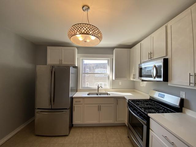 kitchen featuring appliances with stainless steel finishes, sink, pendant lighting, white cabinets, and light tile patterned flooring