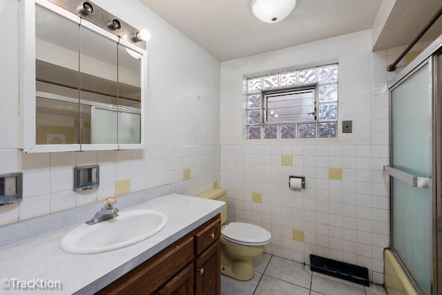 full bathroom with shower / bath combination with glass door, tile walls, vanity, tile patterned floors, and toilet