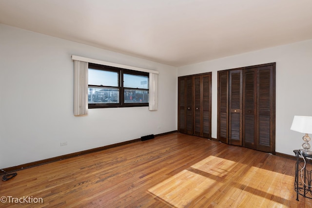 unfurnished bedroom with hardwood / wood-style floors and two closets