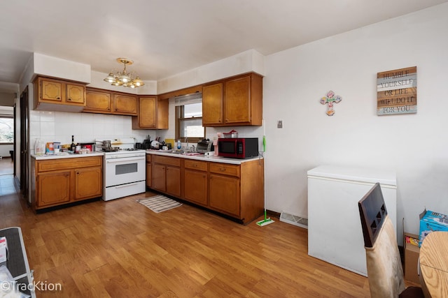 kitchen featuring sink, white range with gas cooktop, an inviting chandelier, and light wood-type flooring