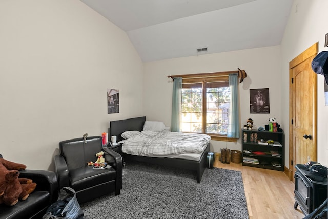 bedroom featuring light hardwood / wood-style floors, a wood stove, and lofted ceiling