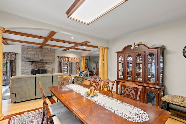 dining space with coffered ceiling, a stone fireplace, ornate columns, beamed ceiling, and light hardwood / wood-style floors