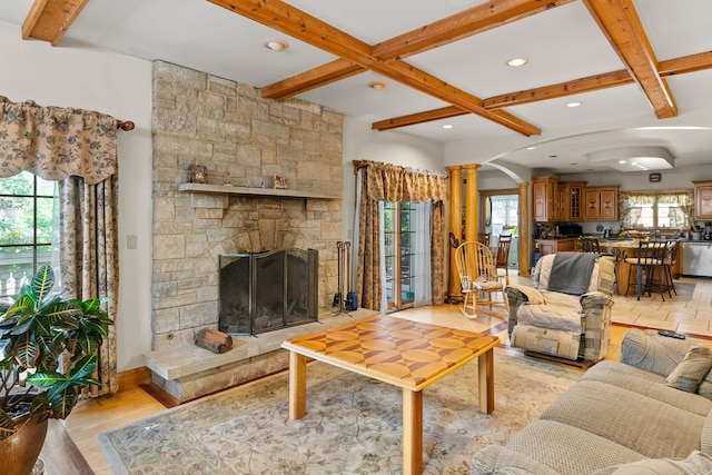 living room featuring decorative columns, a stone fireplace, coffered ceiling, and light hardwood / wood-style floors