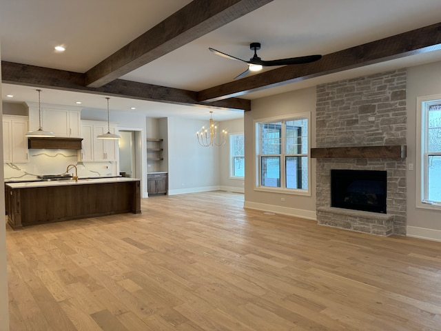 kitchen featuring pendant lighting, light hardwood / wood-style floors, decorative backsplash, a fireplace, and ceiling fan with notable chandelier