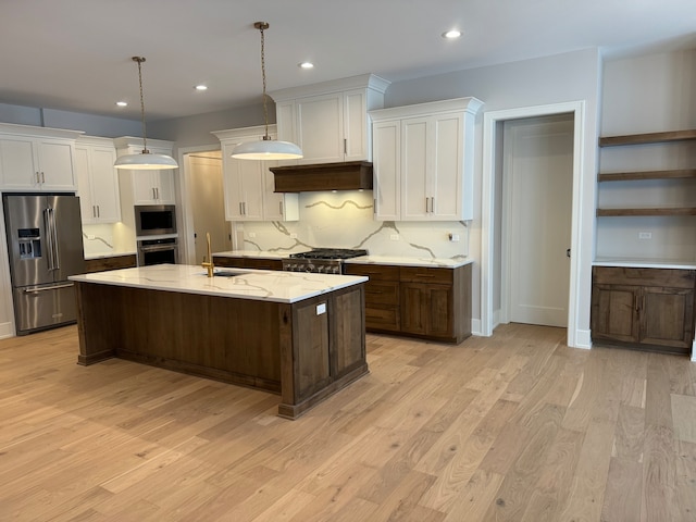 kitchen featuring light stone countertops, stainless steel appliances, decorative light fixtures, a center island with sink, and light wood-type flooring