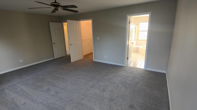 unfurnished bedroom featuring dark colored carpet, connected bathroom, ceiling fan, and a walk in closet