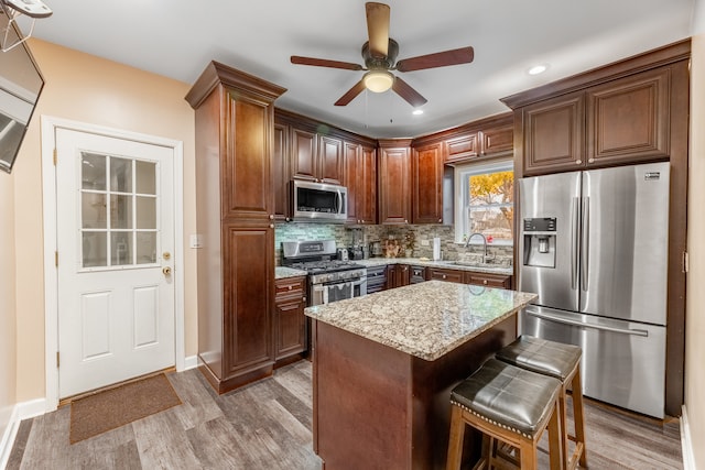 kitchen featuring sink, light hardwood / wood-style floors, appliances with stainless steel finishes, a kitchen island, and light stone counters