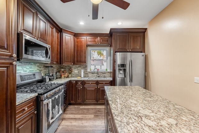 kitchen with backsplash, light stone counters, stainless steel appliances, sink, and light hardwood / wood-style flooring