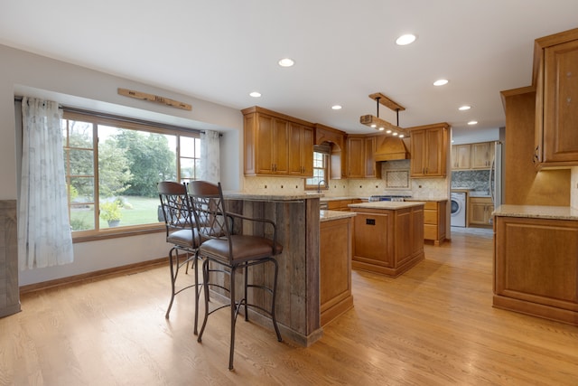 kitchen featuring a center island, hanging light fixtures, light wood-type flooring, light stone counters, and washer / clothes dryer